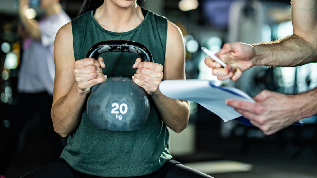 Person performing kettlebell exercise with coach guidance in a strength training gym
